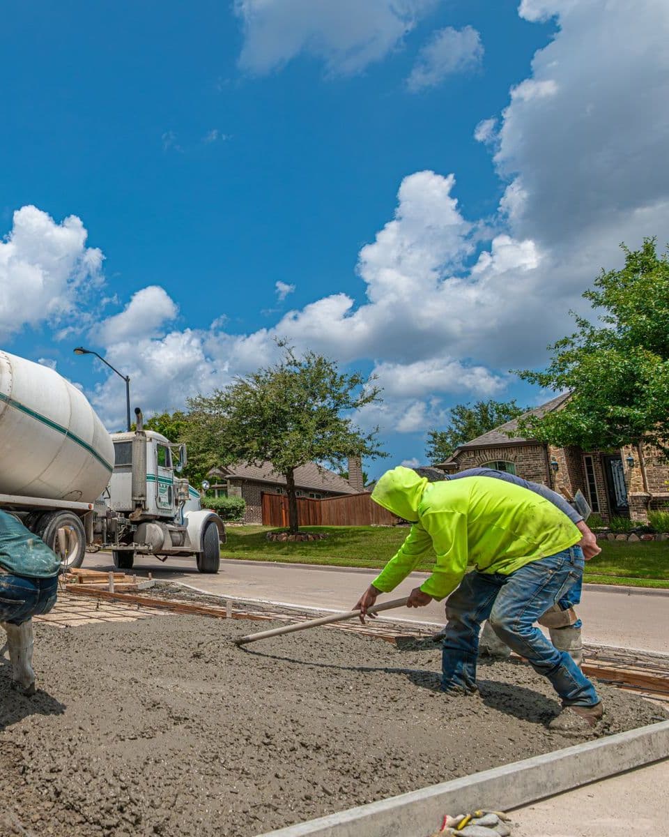 Crew spreading freshly poured concrete for a driveway next to a mixer truck