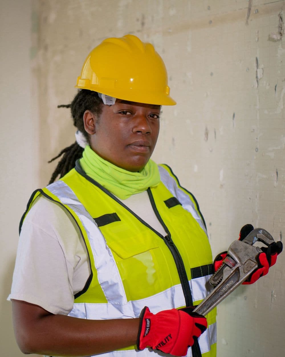 Plumber in a hard hat and safety vest holding a pipe wrench