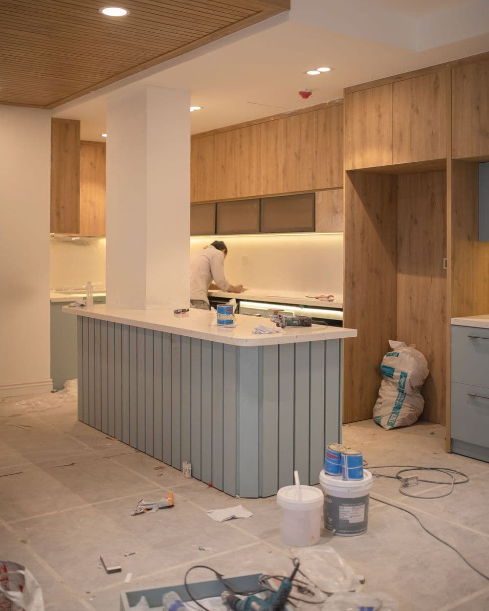 A kitchen renovation in progress with tools on the floor and a worker in the background