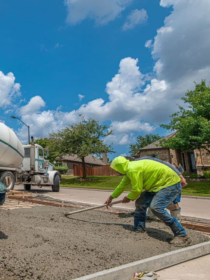 Crew spreading freshly poured concrete for a driveway next to a mixer truck