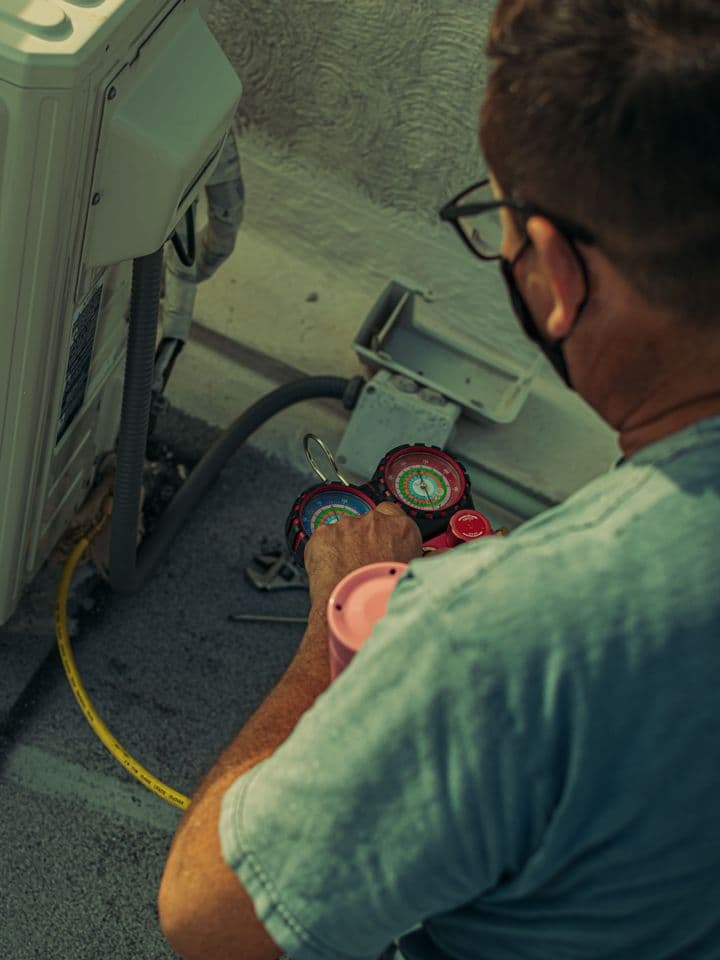 HVAC technician checking an outdoor air conditioning unit with gauges